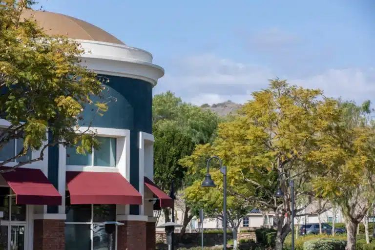 Commercial building with red awnings and surrounding trees in Ladera Ranch, California, on a sunny day.