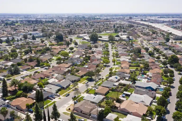 Aerial view of Norwalk, California, showing residential buildings, streets lined with trees, and a mix of urban and suburban areas under a clear sky.